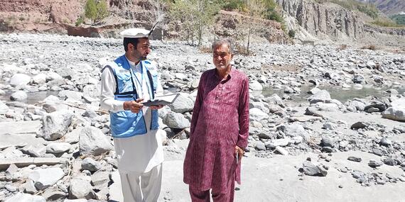 Ali Jabbar (right), whose agricultural land in Pakistan’s Khyber Pakhtunkhwa Province was devastated by flash floods in April 2024, shares his story of loss with UNA-UK staff member Umer Dil. Thousands of people have been affected by the floods that washed away farms, 80 canals and hundreds of fruit plants. Photo: UNA-UK